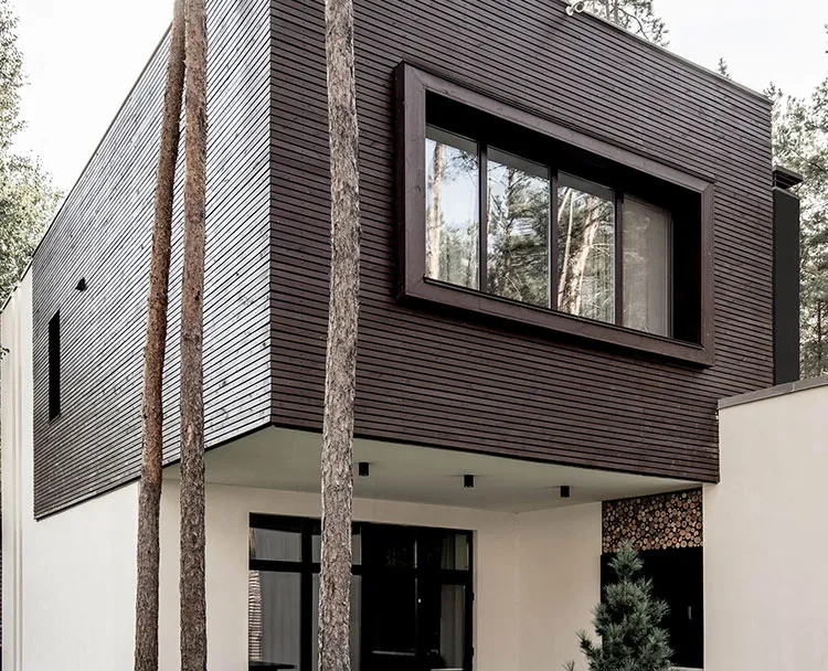 A modern house clad in dark timber, among tall pine trees