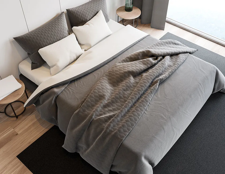 A made bed with grey bedding and cushions, seen from above